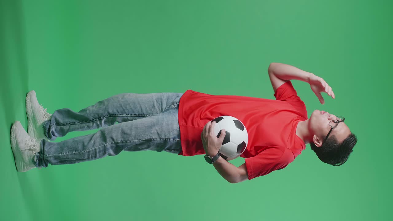 공을 들고 있는 아시아인 남자의 몸은 골을 고 후회하는 동안 녹색 스크린 배경에서 축구를 응원하고 있습니다.