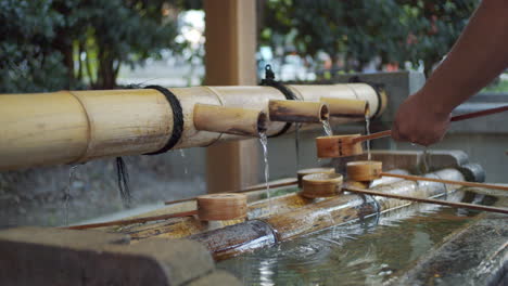 Person-washing-his-hands-early-morning-the-traditional-way,-water-pouring-out-of-bamboo-in-Kyoto,-Japan-soft-lighting