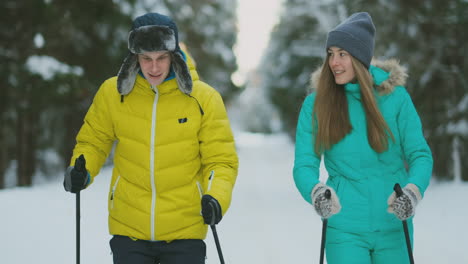 chica sonriente con chaqueta azul esquiando en el bosque con su novio en invierno en vísperas del día de san valentín. camara lenta.