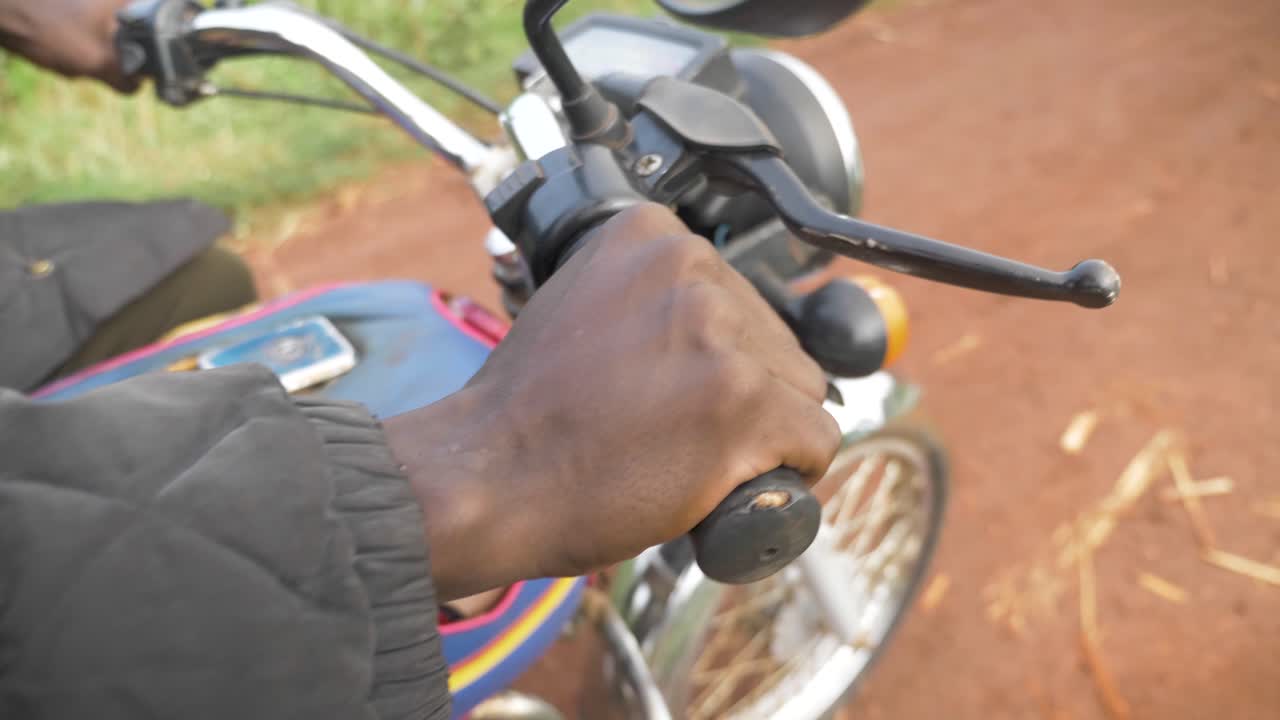 cerca de la mano de un hombre africano acelerando el acelerador de una moto en el áfrica rural