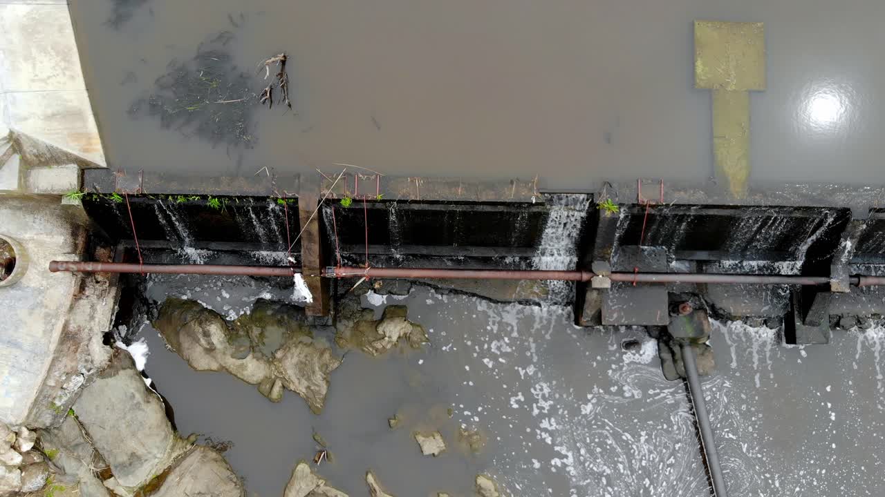 Aerial video moving vertically over the river with a dam running water over the rocks