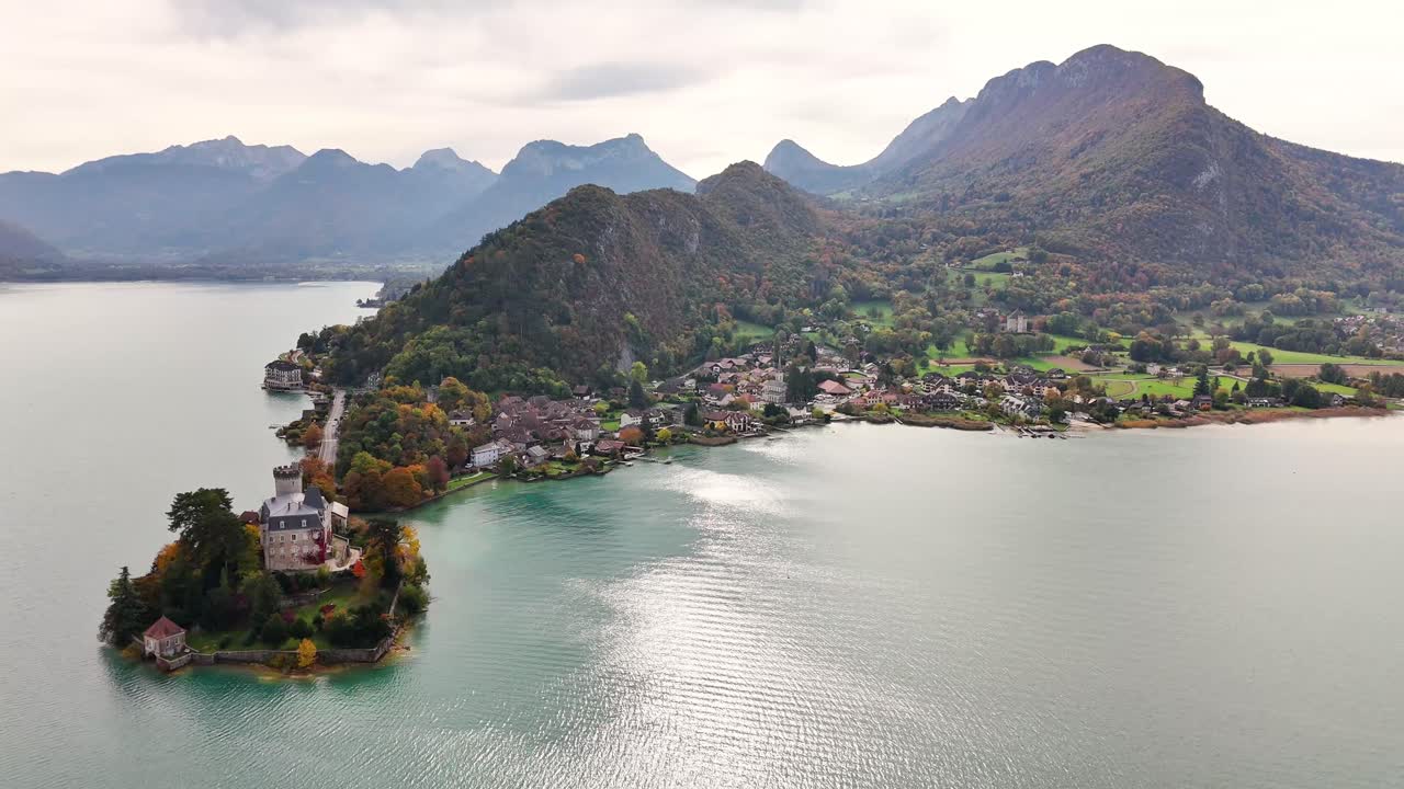 Aerial view of Chateau de Duingt in France on a small peninsula surrounded by calm lake waters, nearby village homes, lush greenery, and towering mountains creating a scenic landscape