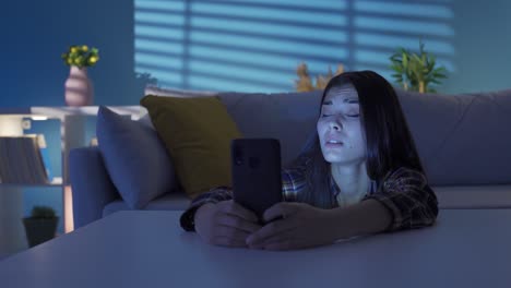 una joven triste sentada en el suelo cerca del sofá mirando el teléfono. enviando mensajes de texto.