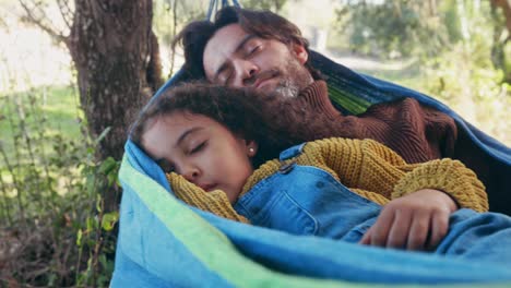 father and daughter sleeping on a hammock in the woods