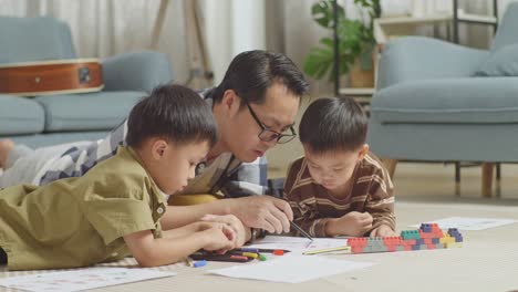 close up of asian father and sons lying on the floor in the room with plastic toy brick. teaching drawing, talking, playing together at home