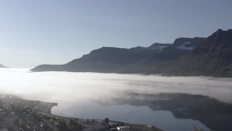 rising above reydarfjordur in east iceland with morning fog above fjord