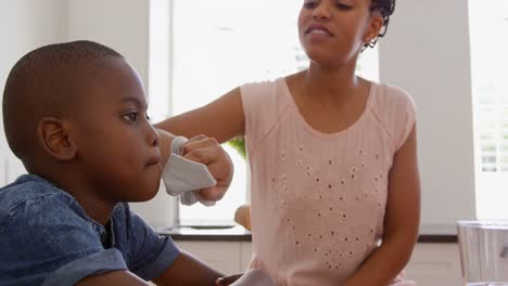 Front-view-of-mid-adult-black-father-wiping-sons-mouth-at-dining-table-in-a-comfortable-home-4k