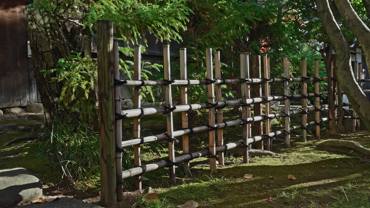 Vista dettagliata di una classica recinzione di bambù Yotsume-gaki (a quattro occhi) che si erge su un terreno coperto di muschio in un tranquillo giardino giapponese