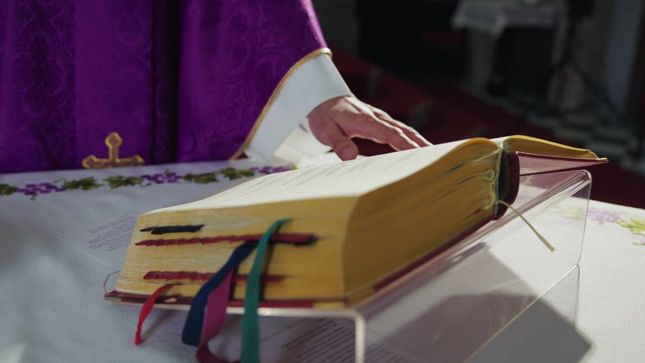 Kněz ve fialovém ornátu (kasuli) listuje stránkami v misálu, liturgické knize