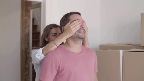 caucasian woman entering into room with husband, opening man's eyes and showing him their new flat