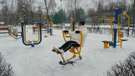 sports ground with diverse simulators in winter. adult woman in white jacket training on snowing weather.