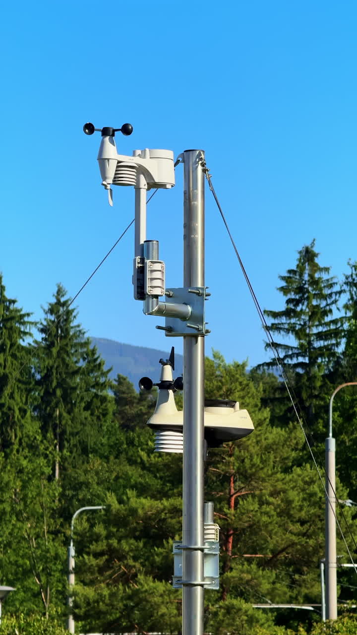 Green area weather station. A weather station rises against a clear sky, surrounded by trees and mountains in the distance