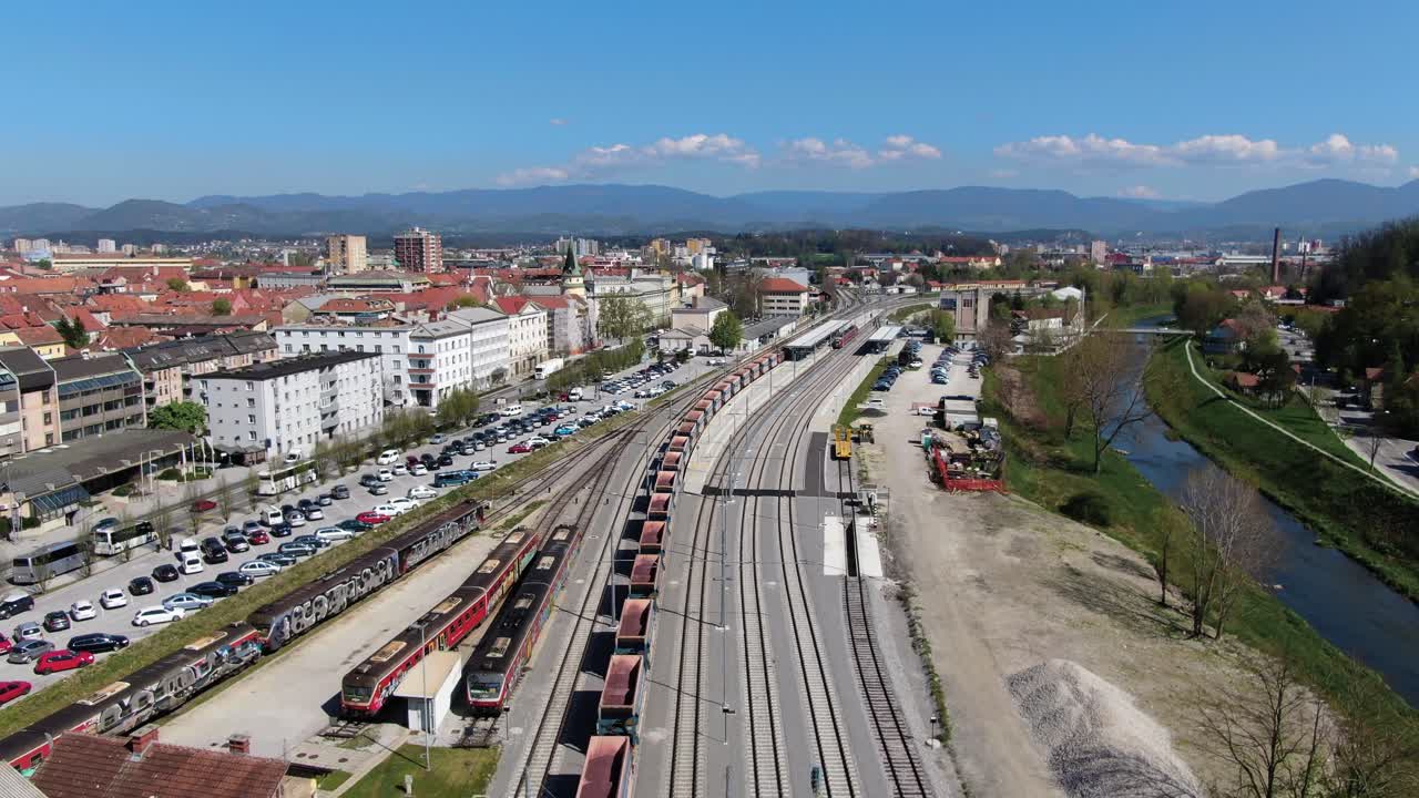 Tracking shot of a freight train driving out of a city along a river at a sunny day