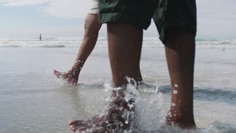 Mixed-race-senior-couple-walking-and-holding-hands-at-the-beach