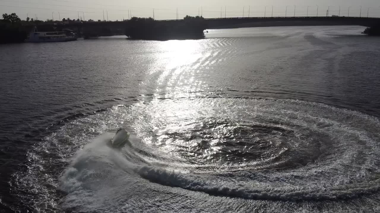 Jetsky is driving in circles on the water and the sun is reflecting on the surface from the water. People having fun.