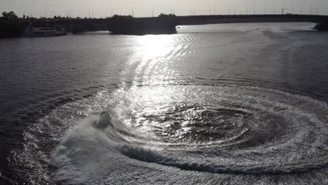 jetsky is driving in circles on the water and the sun is reflecting on the surface from the water. people having fun.