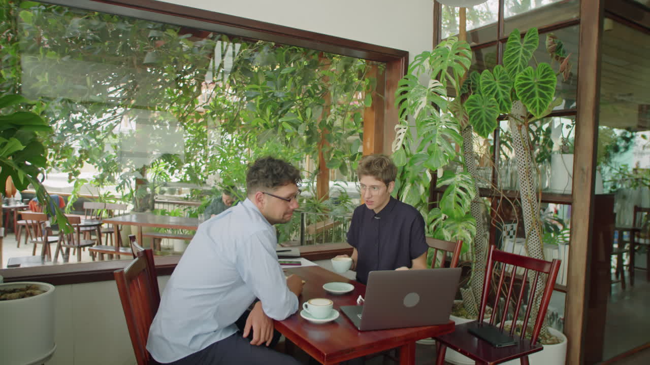 Business People Using Laptop and Talking over Coffee in Outdoor Cafe