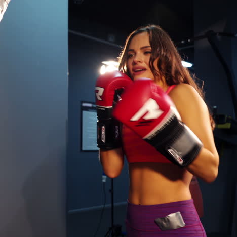 energetic woman wearing gloves in the gym boxing big pear and articulates something with her mouth. concentrated fighter girl confidently punches a pear