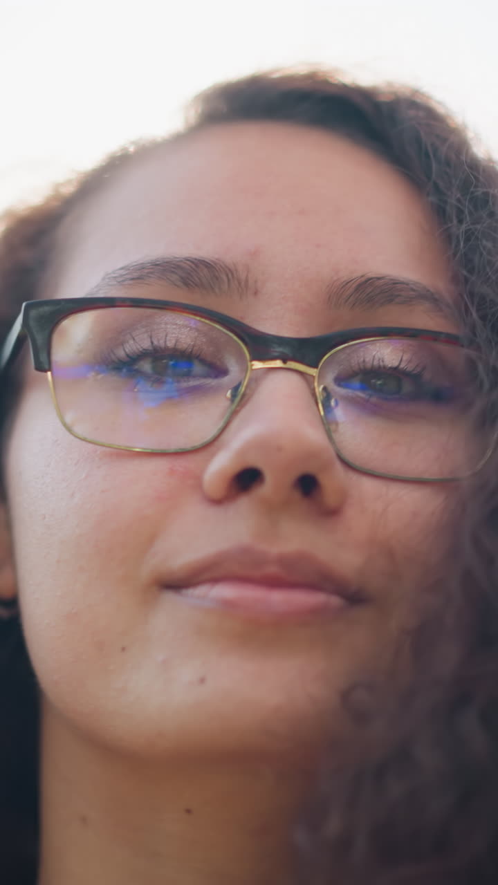 primer plano de una joven con gafas ajustando su cabello mientras sonríe cálidamente, con una suave luz natural iluminando suavemente su rostro, creando una atmósfera elegante y serena