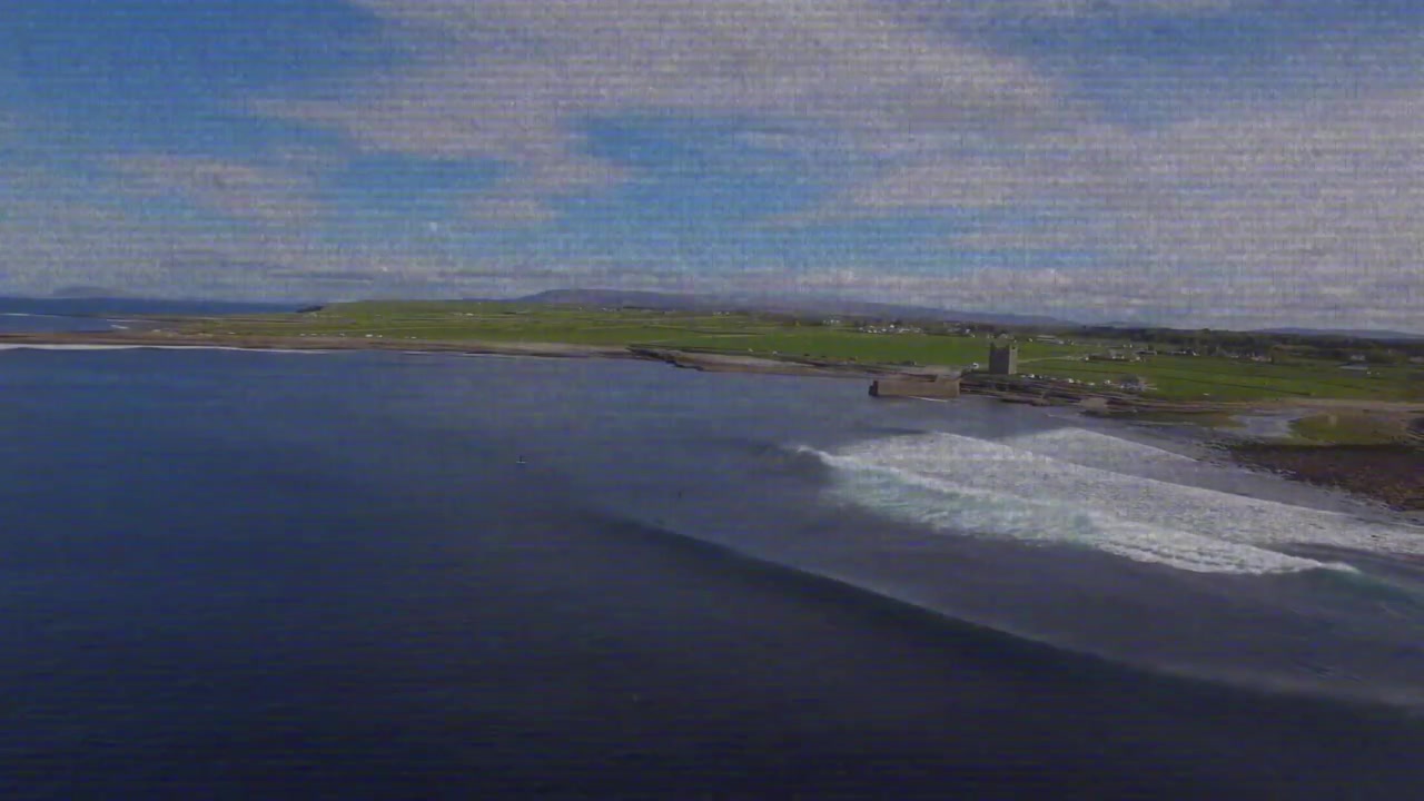 Camera panning, coastline revealing headland and tower while swells breaking, revealing shoreline