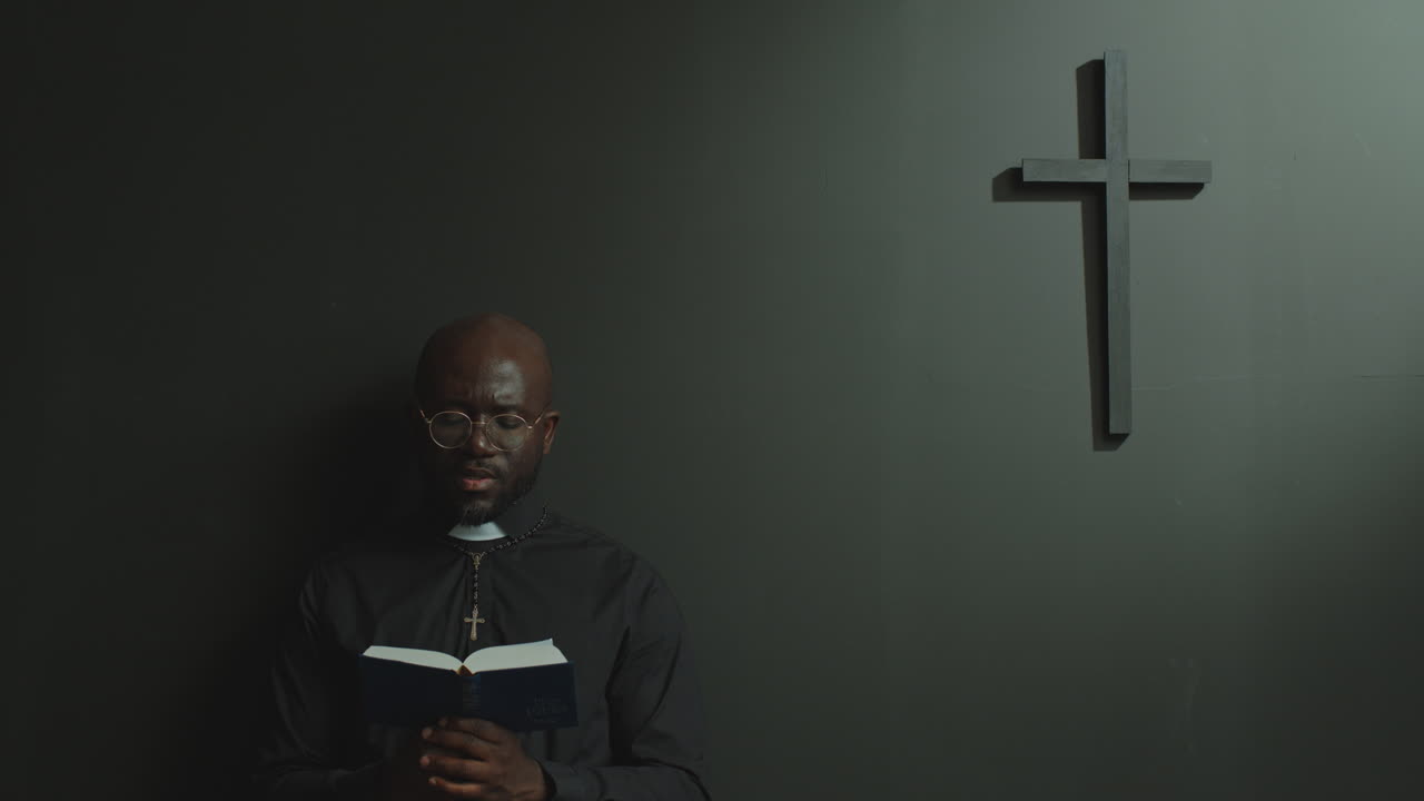 Afroamerický kněz se modlí k Bohu s Biblí v moderním kostele.