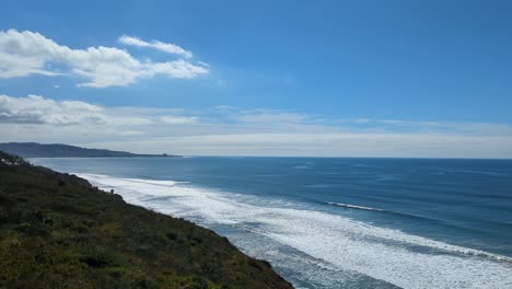 scenic panning view of hiking trail in torrey pines, san diego facing ocean waves crashing against shoreline and blue skies