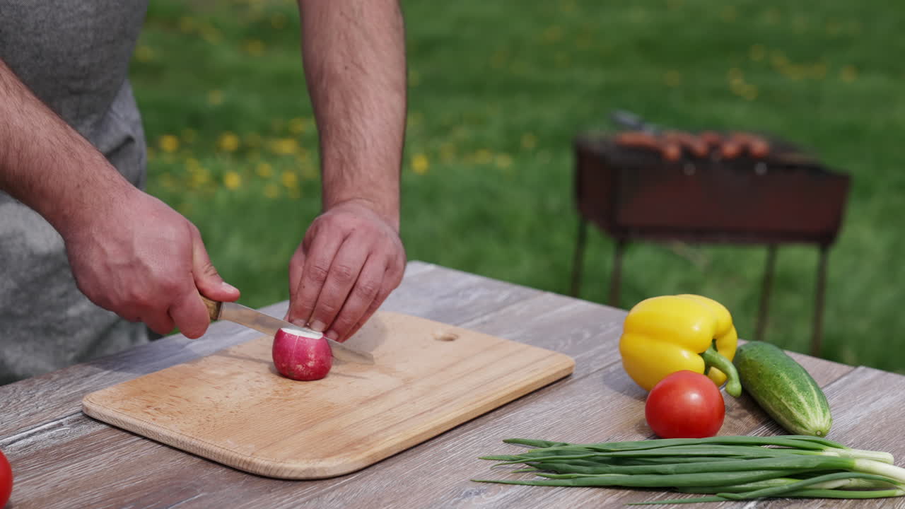 Man cutting radish for a barbeque. Fresh vegetables on the table on the background of a brazel with grilling meat. Time for a picnic.