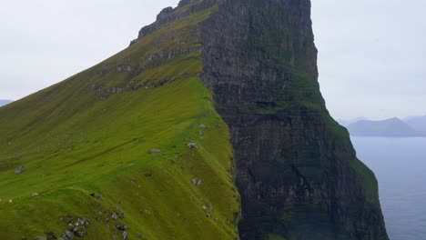 Drone-footage-of-cliffs-near-the-Kallur-Lighthouse-with-mountains-in-the-background-on-the-Kalsoy-island-in-the-Faroe-Islands