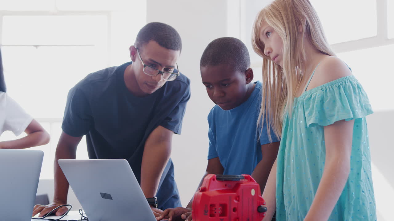 estudiantes con un maestro masculino en una clase de codificación de computadoras después de la escuela aprendiendo a programar un vehículo robot