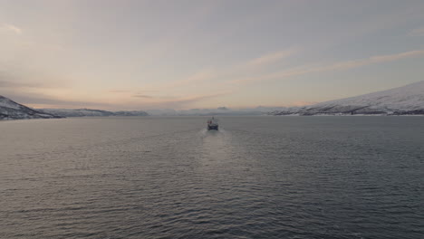 Drone-Following-Cargo-Ship-At-Distance-Across-Fjord-Near-Tromso-In-Norway-At-Sunrise