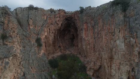 Drohne-Zieht-Aus-Dunkler-Felsenhöhle-Zum-Steilen-Klippeneingang-Der-Höhle,-Israel