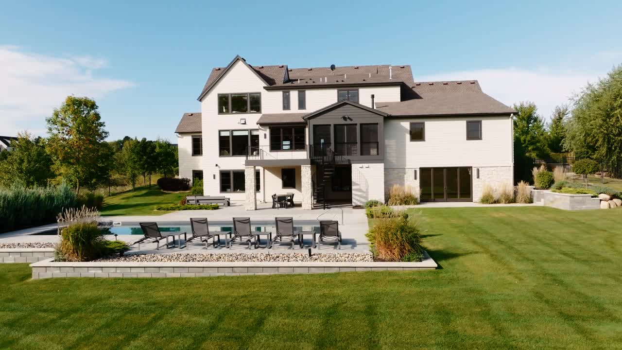 an aerial drone shot of the backyard of a large luxury home with a pool, large backyard, and patio space on a bright sunny day