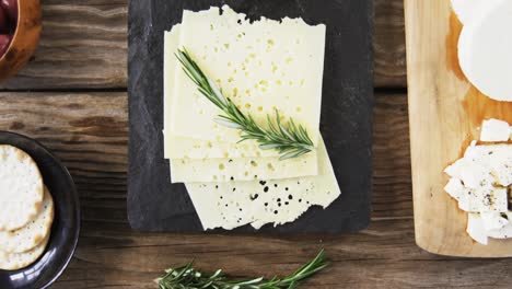 variety of cheese, olives, biscuits and rosemary herbs on wooden table