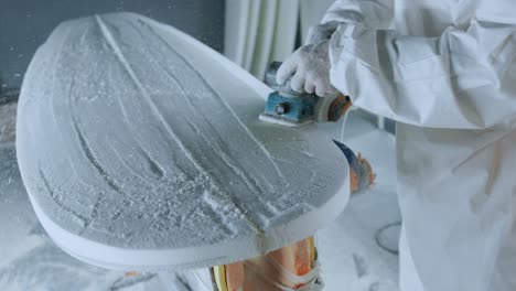 Cropped-anonymous-professional-master-polishing-surfboard-in-workshop