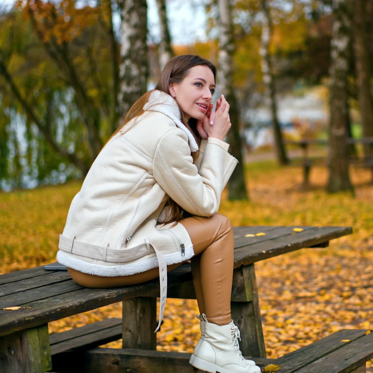Relaxed calm dark-haired lady sits on the table thinking of something. Caucasian girl enjoying beautiful autumn day in the park among birch trees
