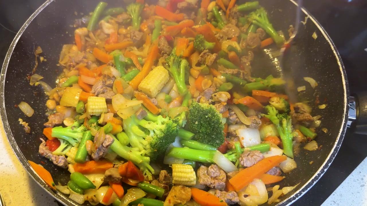 Primo piano di manzo, broccoli e carote che sfrigolano in una padella fumante durante la cottura casalinga.