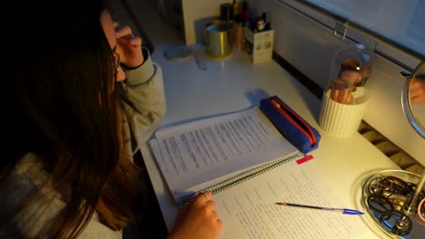 una chica estresada muerde y lanza un bolígrafo mientras estudia tarde en la noche para un examen.