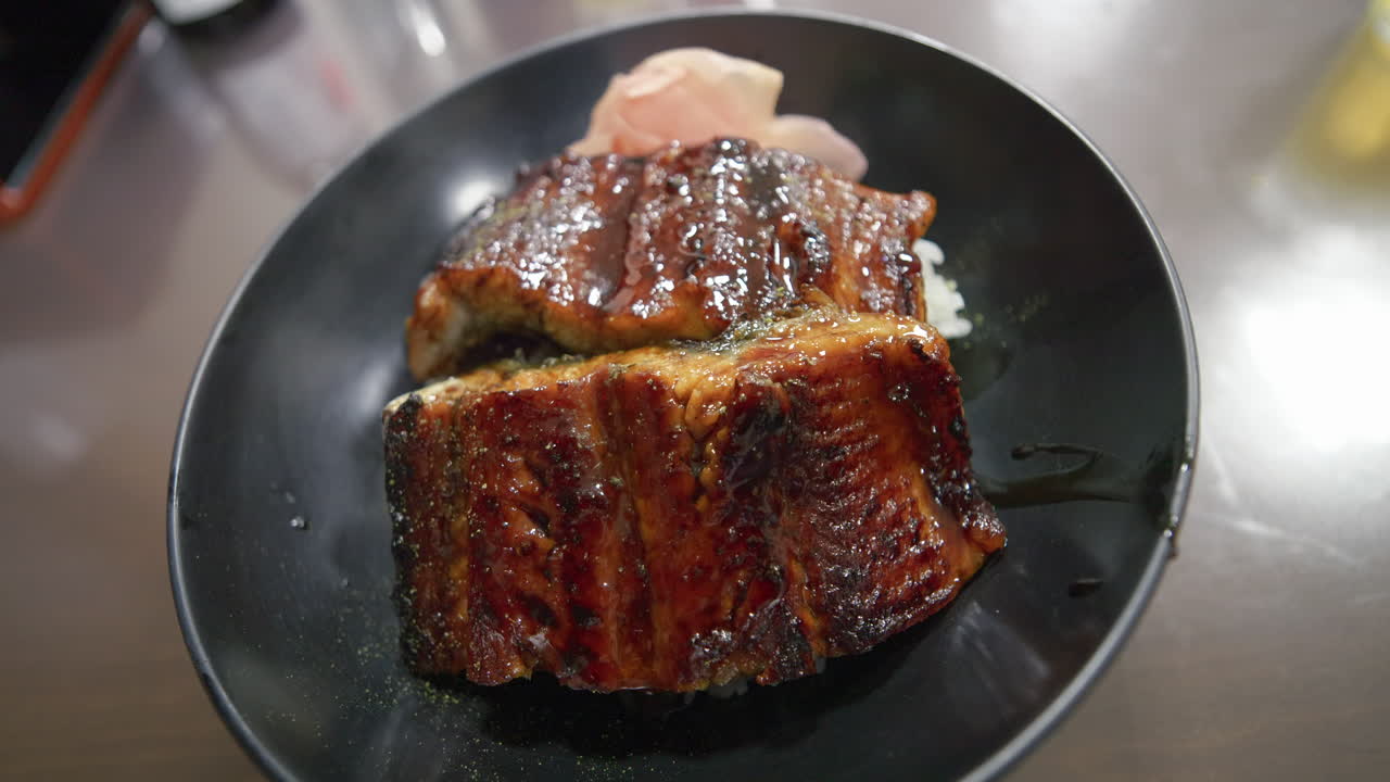 Grillet japansk unagi-ål med blank saus servert på en mørk tallerken, nærbilde.