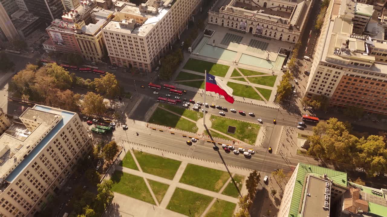 Slow motion aerial of the Bandera Bicentenario, a monumental Chilean flag waving proudly along a busy avenue in de Chile, along with city traffic.