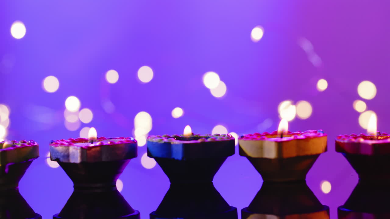 Nærbillede af brændende farverige stearinlys, der fejrer Diwali på lilla baggrund.
