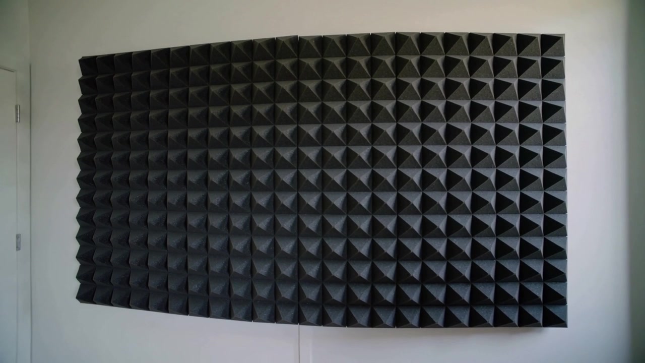 Cámara en movimiento grabando panel de espuma acústica montado en la pared de una habitación, revelando la puerta izquierda y la junta.