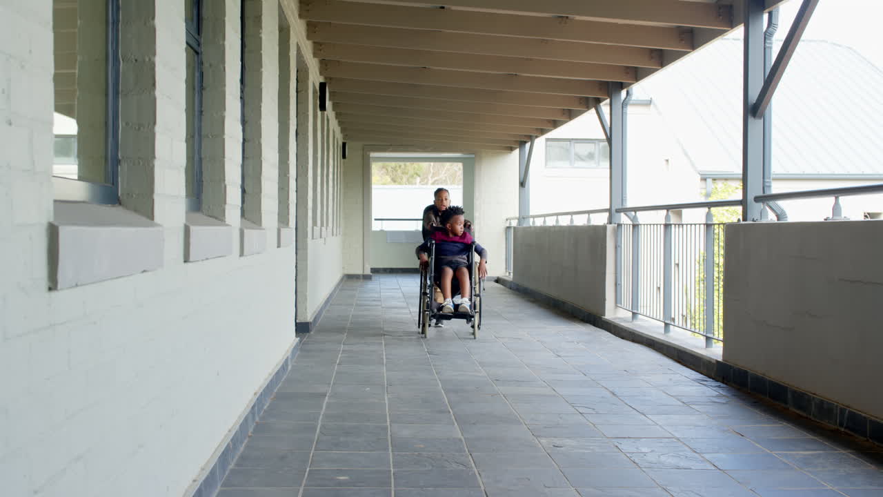Boy in wheelchair being pushed by friend in school hallway, smiling together