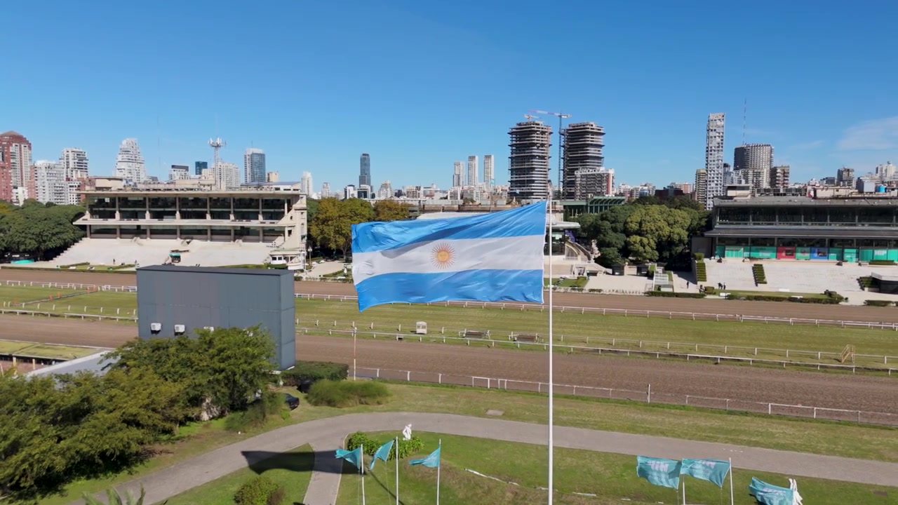 Bandeira argentina tremulando em mastro alto contra o horizonte da cidade e autódromo em dia claro