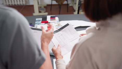 costumiers reviewing different material design patterns during creative brainstorming session, holding pattern sketches on paper while colorful paper sheets are scattered across workspace