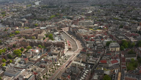 Weitläufige-Luftaufnahme-Des-Stadtzentrums-Von-Amsterdam-In-Richtung-Fluss-Mit-Booten