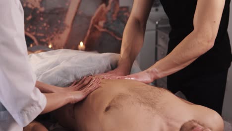 close-up of the hands of a woman and a masseur man doing a four-handed abdominal massage of a man with an athletic physique