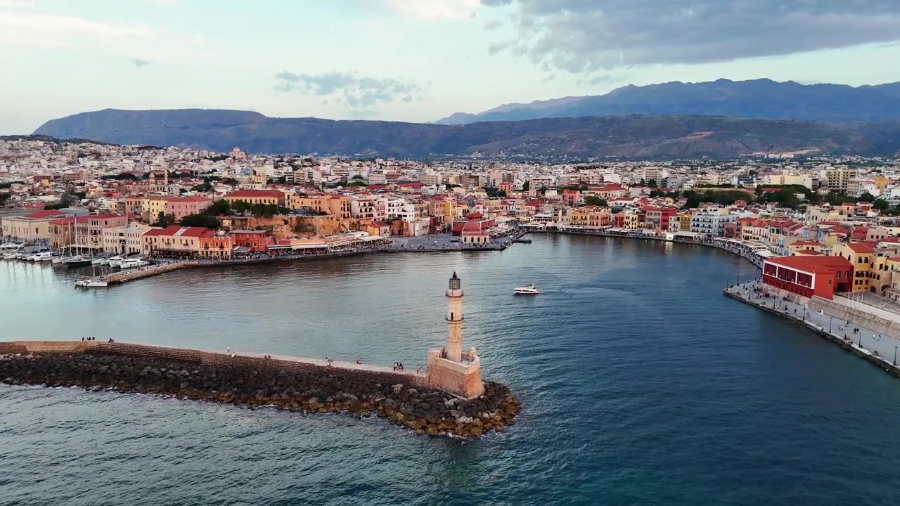 Il Vecchio Porto Veneziano di Chania presenta il Faro Egiziano, il lungomare veneziano e le fortificazioni storiche sotto le montagne cretesi, orbita di parallasse con drone