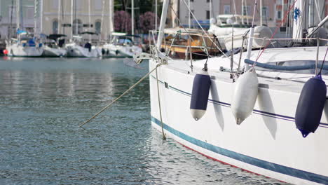 a white sailboat moored in the port of piran with white and blue buoys on the side