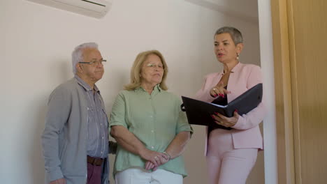 real estate agent holding file and discussing details of sale with senior couple indoors