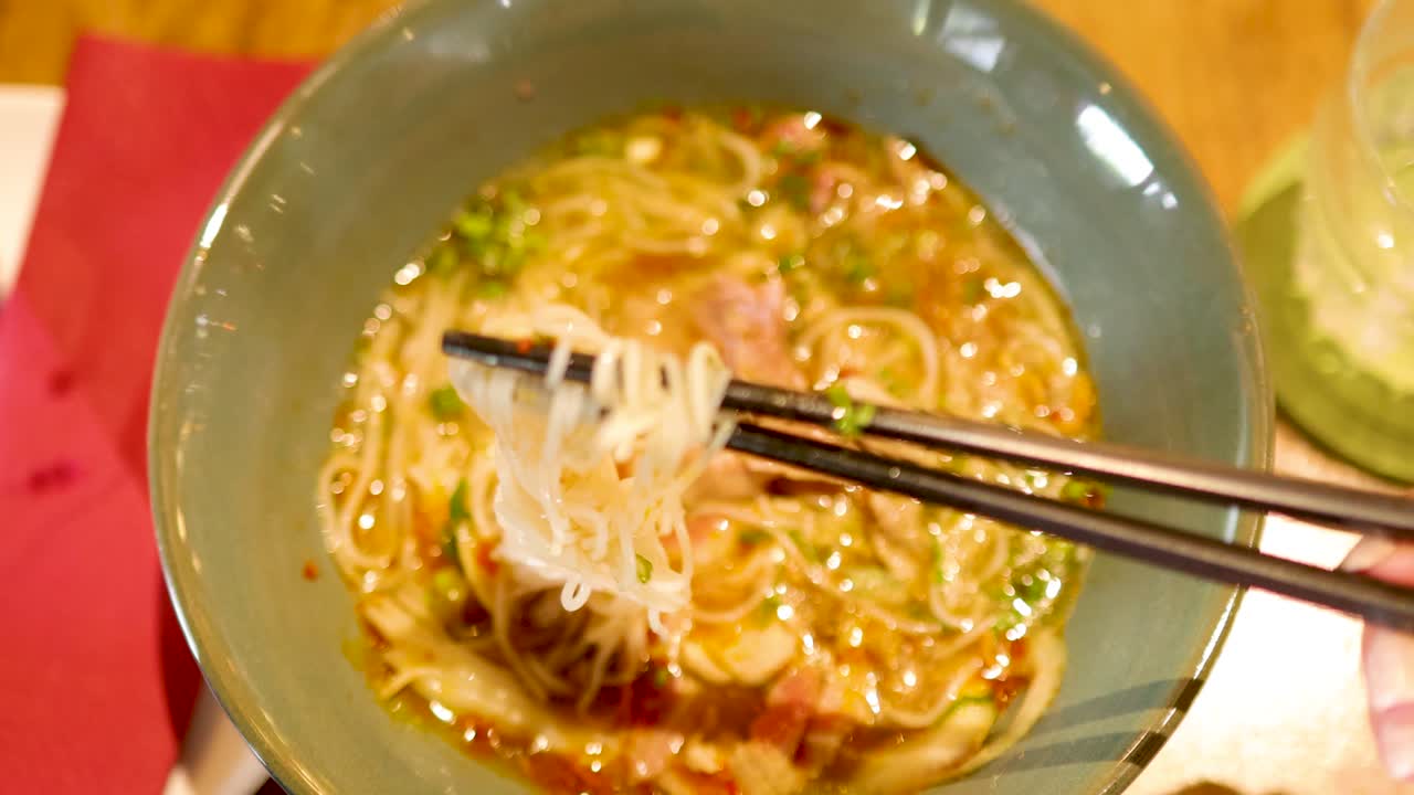 Chopsticks lift noodles from a flavorful Vietnamese soup bowl in a warmly lit Bangkok restaurant